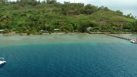 Flying-along-the-tropical-coastline-and-jungles-of-the-Tahitian-island-of-Bora-Bora,-featuring-crystal-clear-blue-green-waters-above-the-reefs