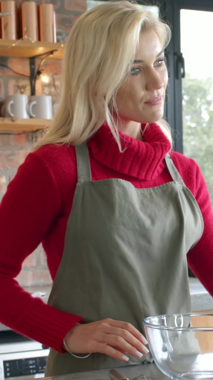 Vertical video: Placing bowl, cook in red sweater, olive apron presenting recipe at kitchen counter