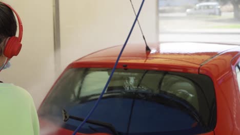 mujer limpiando auto rojo con máscara mientras escucha música, nueva normalidad