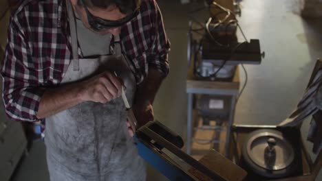 caucasian male knife maker in workshop wearing glasses and using sander