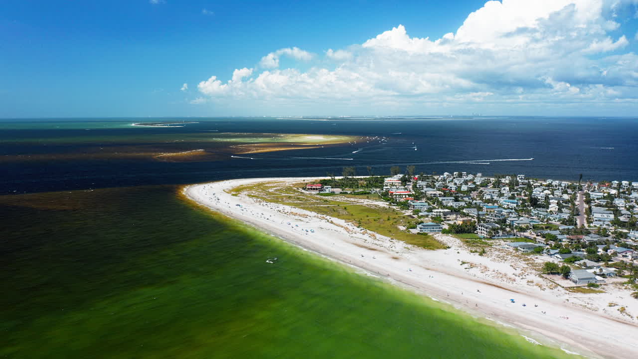 A sandy peninsula lined with homes meets emerald-green shallows and offshore deep waters, showing the intersection of human settlement with expansive marine landscapes