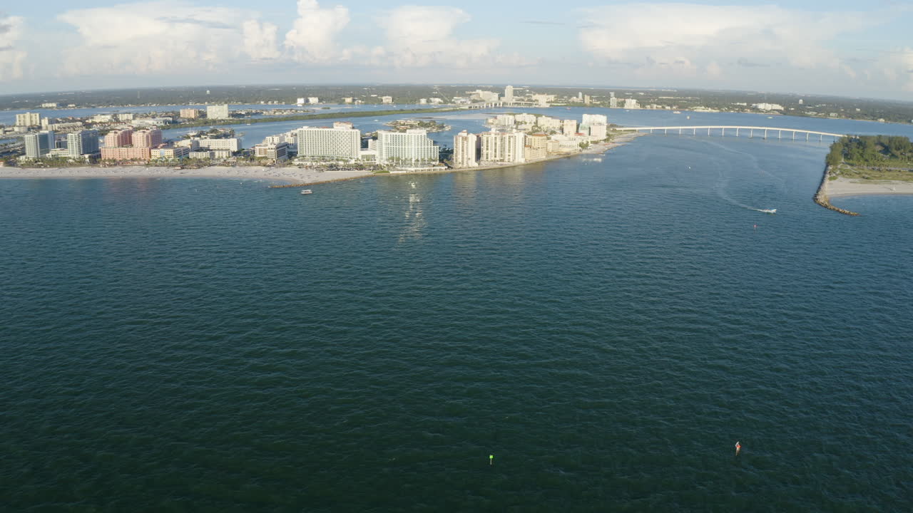 Broad aerial view captures Clearwater Beach’s hotel skyline, sandy shoreline, and sweeping gulf waters with the bay bridge stretching across the horizon, conveying scale and coastal energy