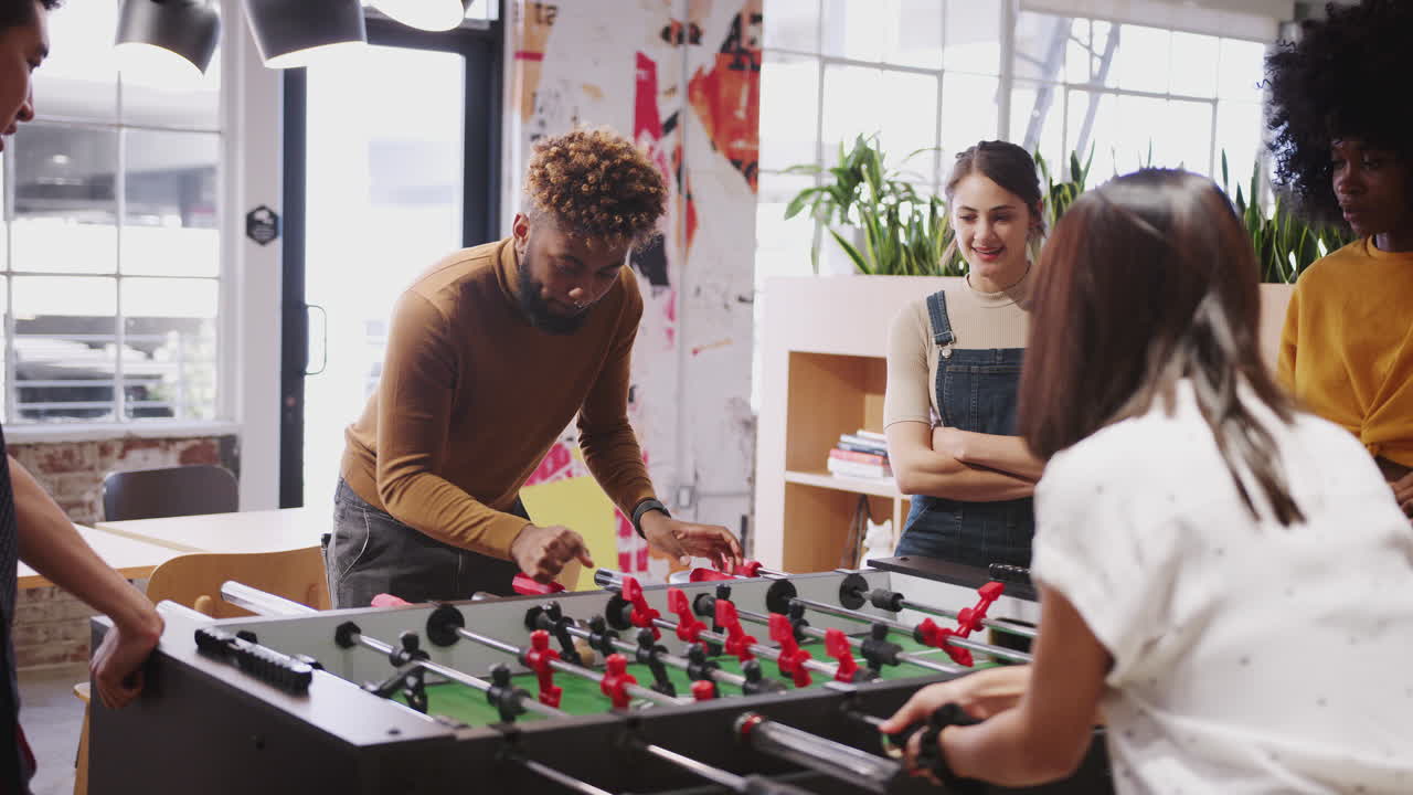 Millennial business creatives take a break playing table football at work