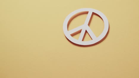 Close-up-of-white-peace-sign-and-copy-space-on-yellow-background