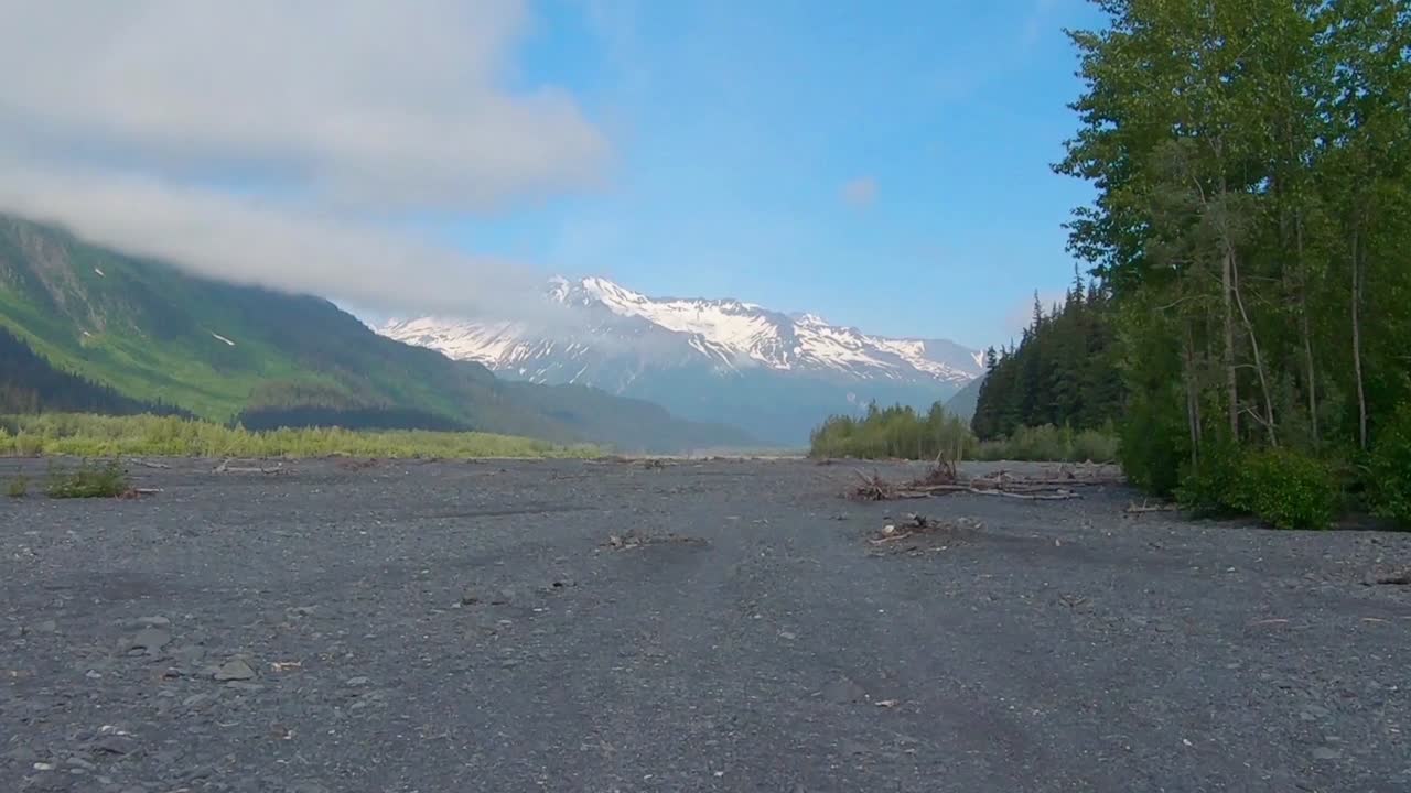 POV through rear window while driving along Exit Glacier moraine and the Resurrection River bed on a sunny after noon near Seward Alaska; Kenai Mountains are visible in the background