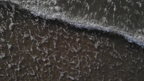 top down view of foamy sea waves washing on the shore at the beach near brouwersdam, netherlands - aerial drone shot