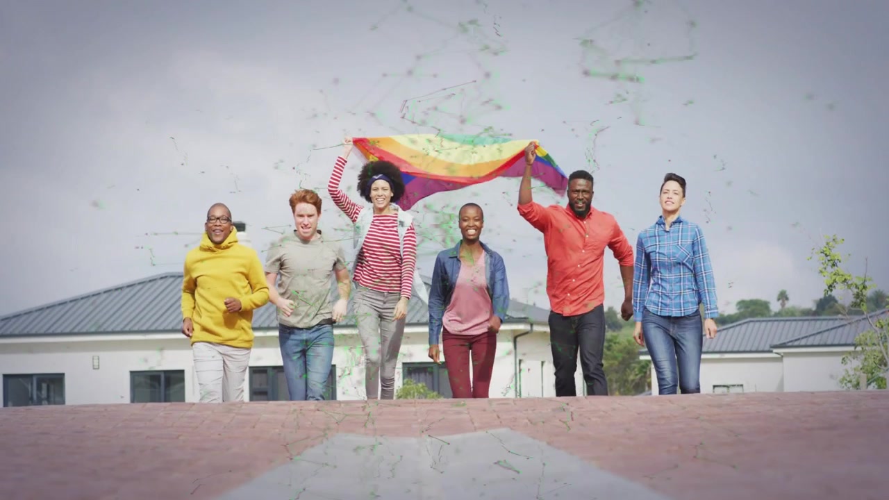 Grupo de seis adultos correndo ladeira abaixo em direção à câmera após levantar a bandeira do arco-íris, celebrando o orgulho.