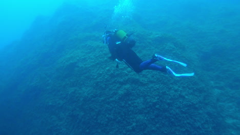 Female-scuba-diver-swiming-towards-a-gap-between-two-rocks-on-a-dive-at-Mallorca,-Spain