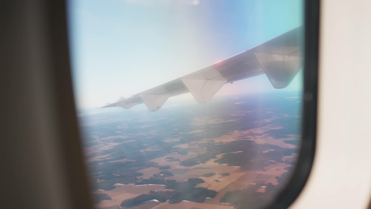 Håndholdt udsigt fra flyvindue med vingen, der løfter sig opad over landbrugsland, fanger bevægelse under flyvning, passagerperspektiv og et autentisk øjeblik fra en kommerciel flyvning.