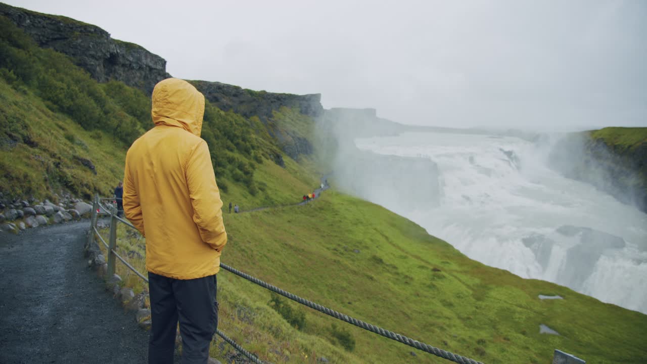 turista masculino con impermeable amarillo en la cascada de gullfoss en islandia en la naturaleza islandesa.