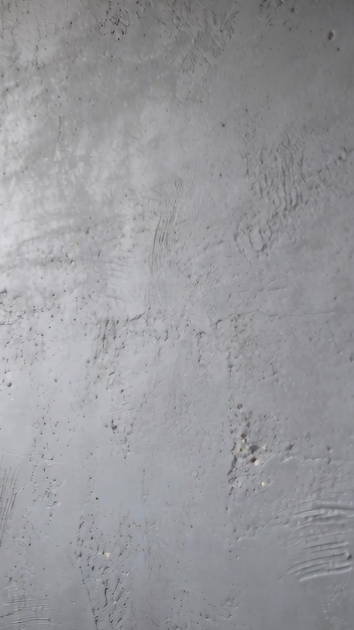 Vertical video: Camera recording textured concrete ceiling showing trowel marks and dust indoors