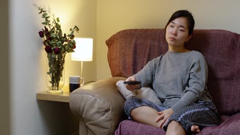 bored asian woman watching tv in self-isolation during corona virus