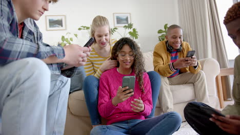 happy diverse group of teenage friends using smartphones and laughing at home, slow motion