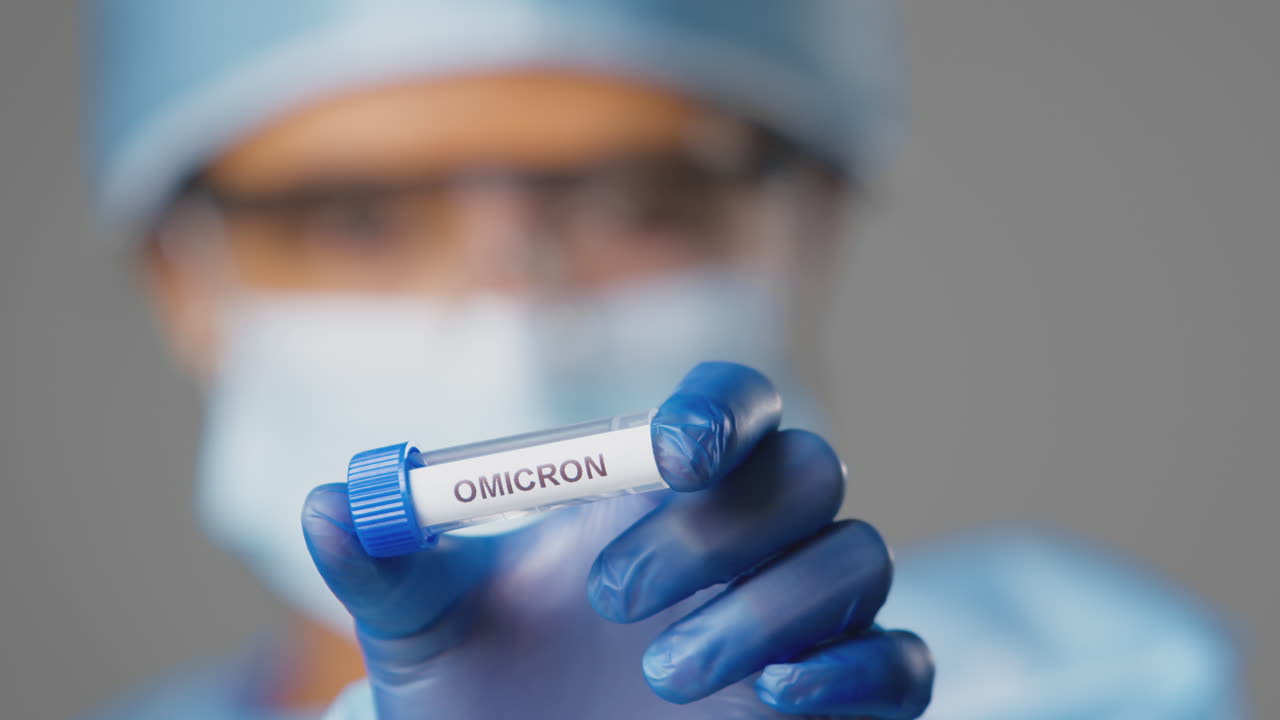 Close Up Of Female Lab Research Worker Wearing PPE Holding Test Tube Labelled Omicron