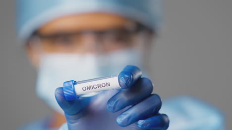 close up of female lab research worker wearing ppe holding test tube labelled omicron