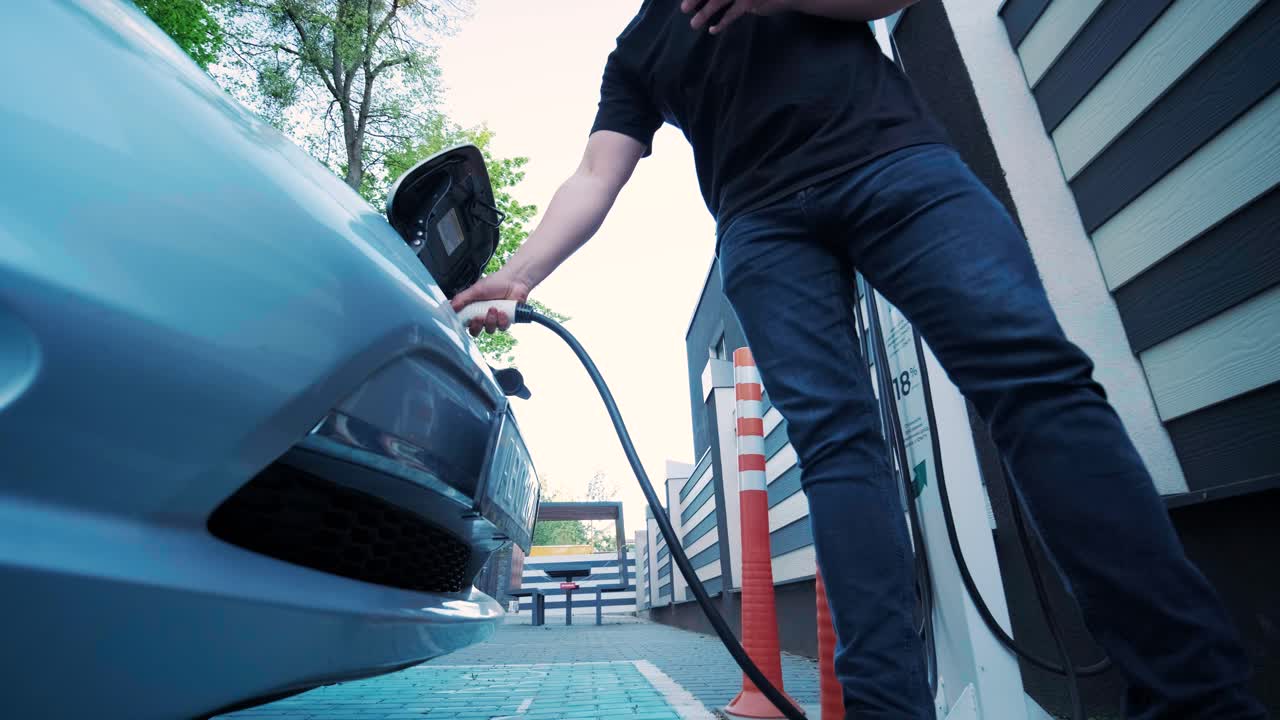 proceso de reabastecimiento de combustible de un automóvil eléctrico. un disparo debajo de la escotilla donde se carga el automóvil ecológico eléctrico. la escotella de carga del automóvil eléctrico se abre automáticamente. una mano masculina inserta un automóvil erecto