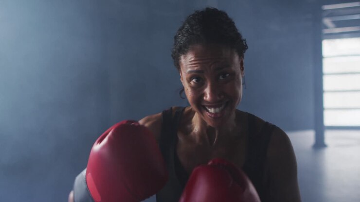 Donna afroamericana con guantoni da boxe che si allena sferrando pugni in una stanza vuota.