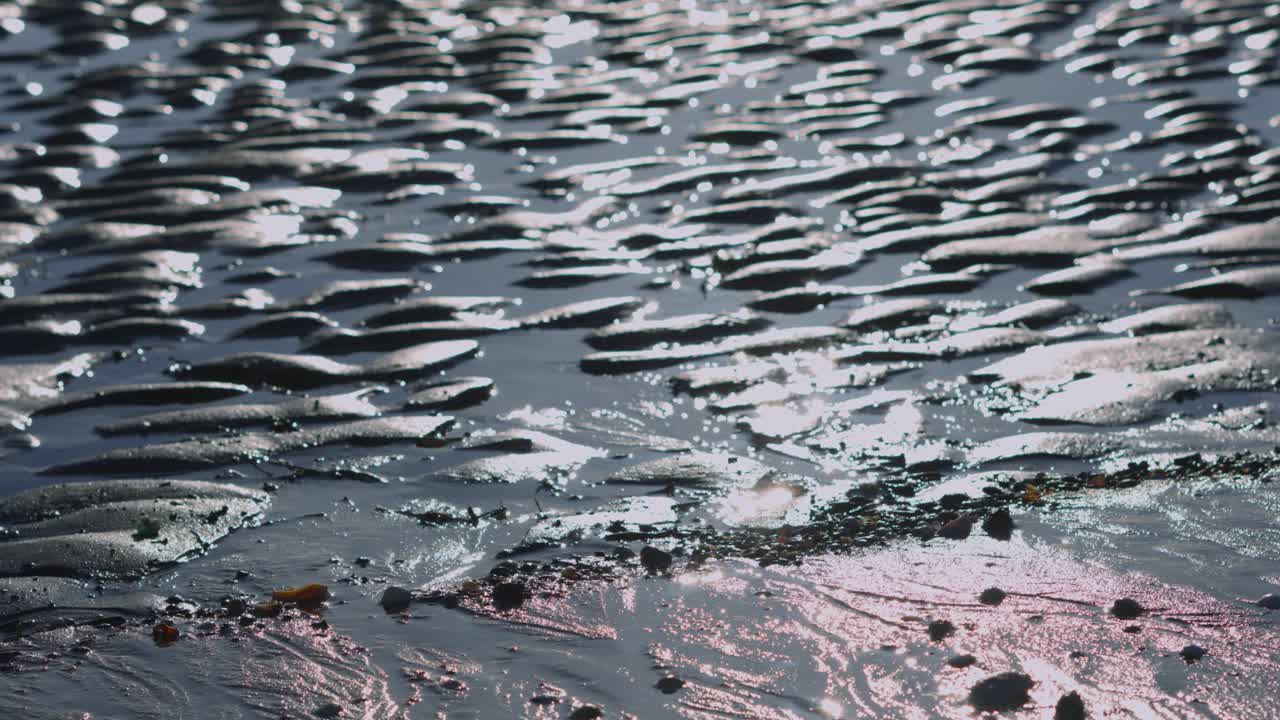Pan Up Over Swansea Bay at Low Tide with Mumbles Ligthouse and Pier Visible on Silhouetted Horizon with Orange Golden Sky Over Ocean 4K