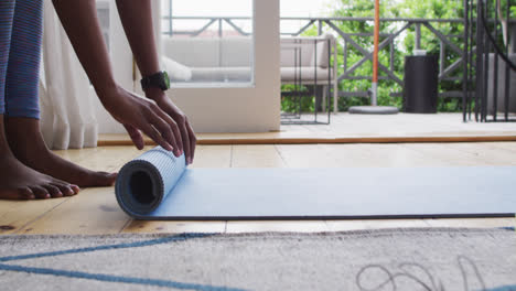 mid section of african american woman rolling yoga mat at home