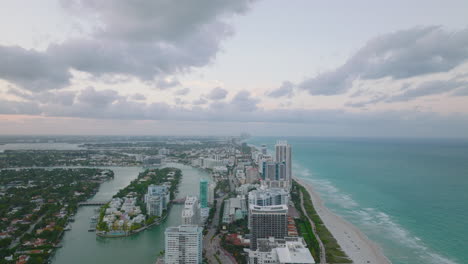 Aerial-panoramic-footage-of-modern-urban-borough-on-sea-coast.-Stripe-of-high-rise-buildings-between-sea-and-river-at-twilight.-Miami,-USA