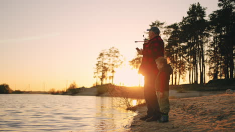 Feliz-Abuelo-Y-Nieto-Están-Pescando-En-La-Orilla-Del-Río-En-Un-Pintoresco-Paisaje-Natural-Con-Pinos