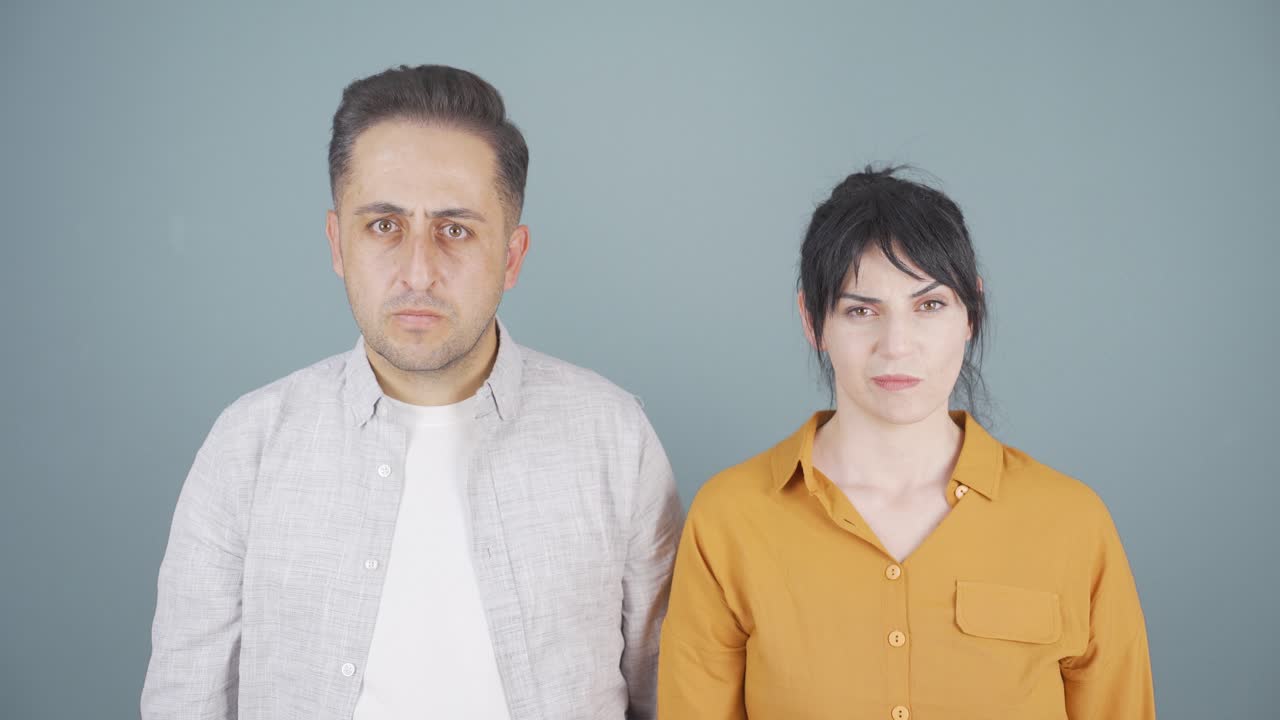 la pareja está mirando a la cámara y haciendo una señal de silencio.