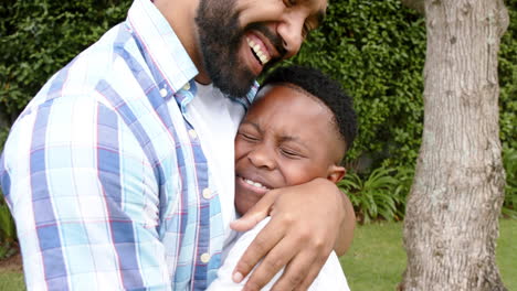 happy african american father and son hugging and smiling in garden, slow motion