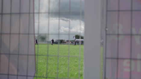 Grupo-De-Hombres-Corriendo-En-El-Campo-Verde-Y-Tirando-De-La-Pancarta-Vista-A-Través-De-La-Cerca-De-Malla-De-Alambre-Soldado-En-Cornualles,-Inglaterra,-Reino-Unido