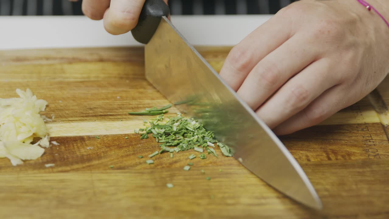 Slicing green spice with kitchen knife on wooden cutting board