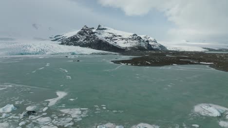 Wunderschöne-Landschaft-Eines-Zugefrorenen-Sees-Und-Schneebedeckter-Berge-In-Island,-Aus-Der-Luft