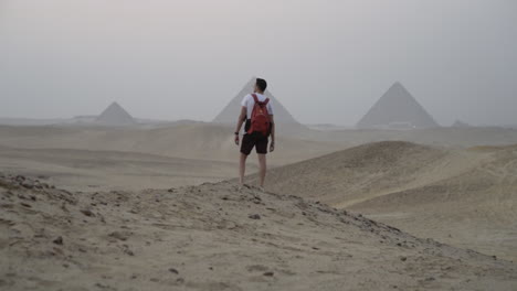 Man stands in desert looking out at Giza pyramids in distance, slow motion