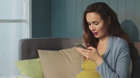 macro pregnant woman touching phone screen on couch at home.