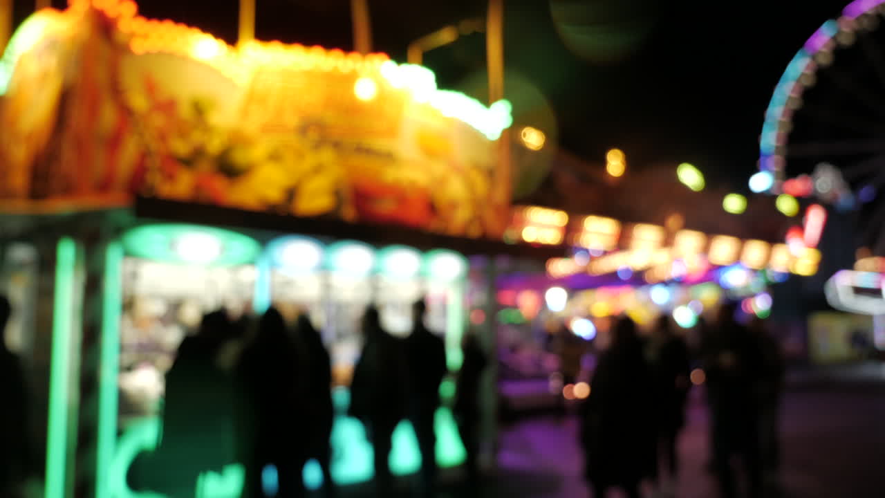 Slow panning right shot,showing people walking on fairground at night,blurred footage