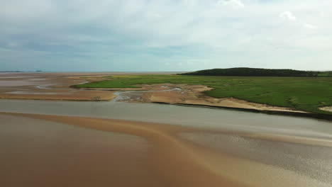 Toma-Aérea-Baja-Sobre-Arena-Dorada-Húmeda-Durante-La-Marea-Baja,-Que-Muestra-Los-Patrones-Naturales-Que-Quedan-Atrás