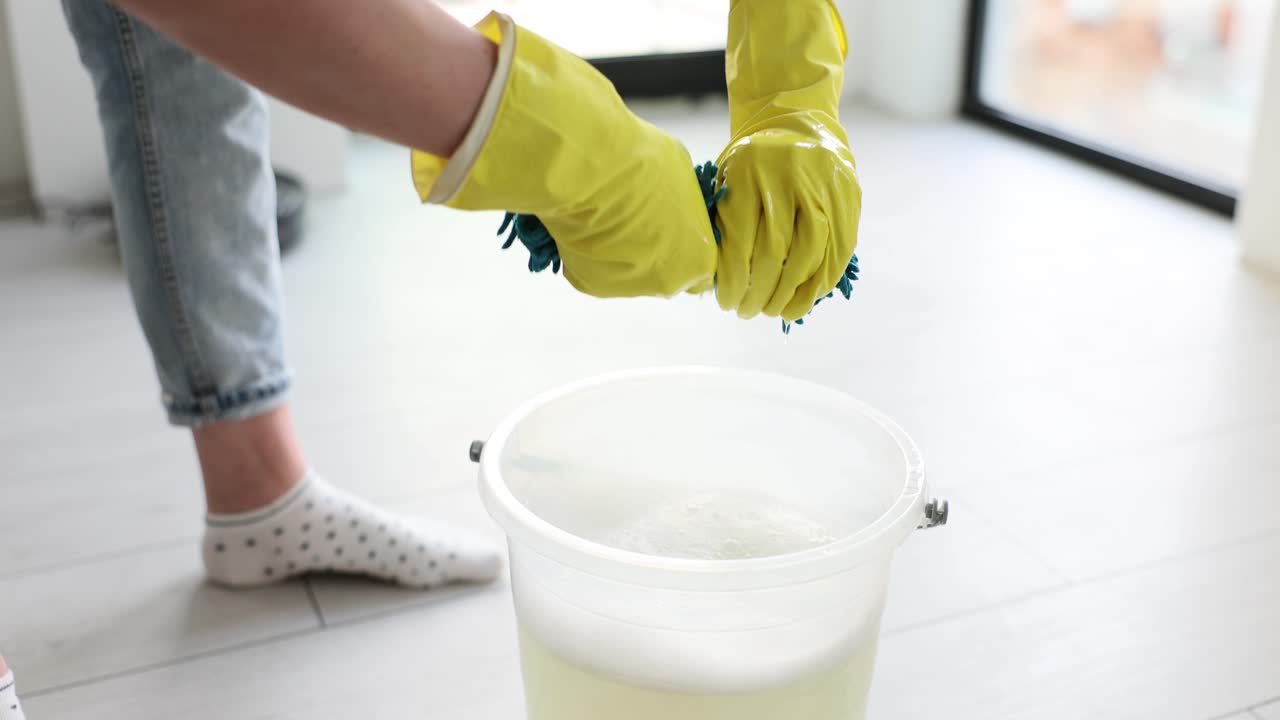 Person wringing out a wet mop into a bucket during cleaning