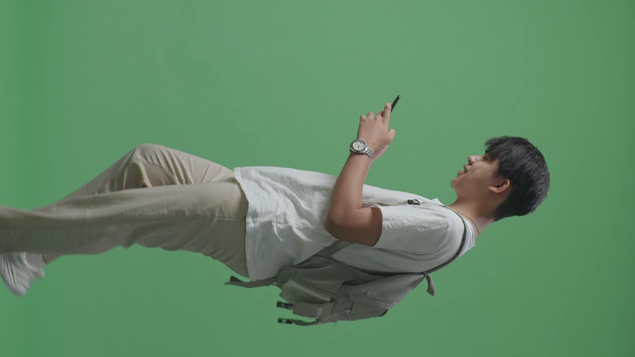 초록색 스크린 스튜디오에서 는 동안 휴대전화를 사용하는 행복한 아시아 남성 학생의 측면 시각