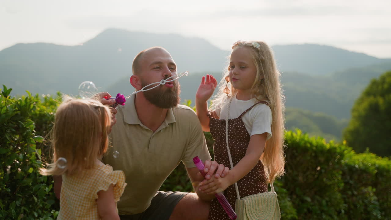 아버지와 딸들이 자연에서 거품을 불고 있습니다.