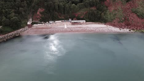 Aerial-backwards-flight-showing-Oddicombe-beach-with-overgrown-cliff-wall-in-Torquay-City,-England