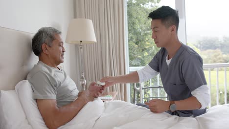 diverse male doctor and senior male patient discussing in bed at home, slow motion