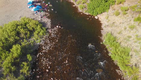 Fliegen-über-Ein-Schwimmloch-Bis-Zu-Einer-Brücke-Im-American-River-In-Auburn,-Kalifornien---Umgeben-Von-Grünen-Bäumen,-Bergen-Und-Voller-Menschen,-Die-Schwimmen-Und-Ihr-Sommerwochenende-Genießen