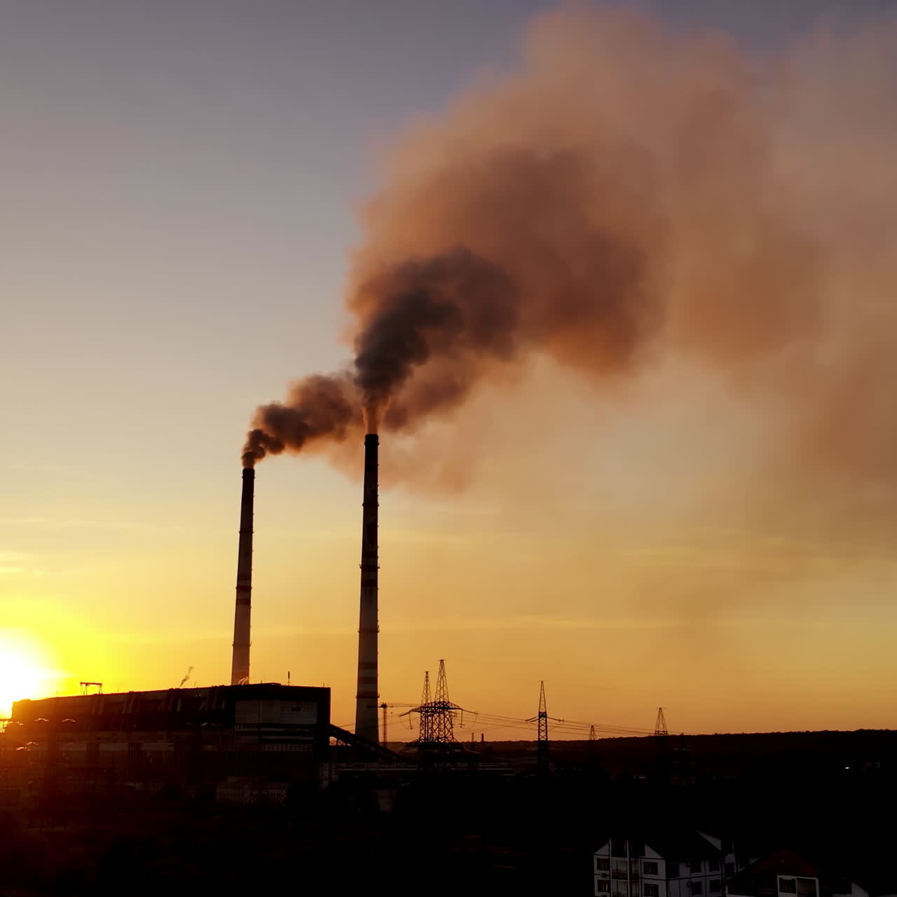 Dark industrial factory in the evening. Metallurgical plant. Smoke coming out of factory pipes at sunset. Drone view. Motion camera back.
