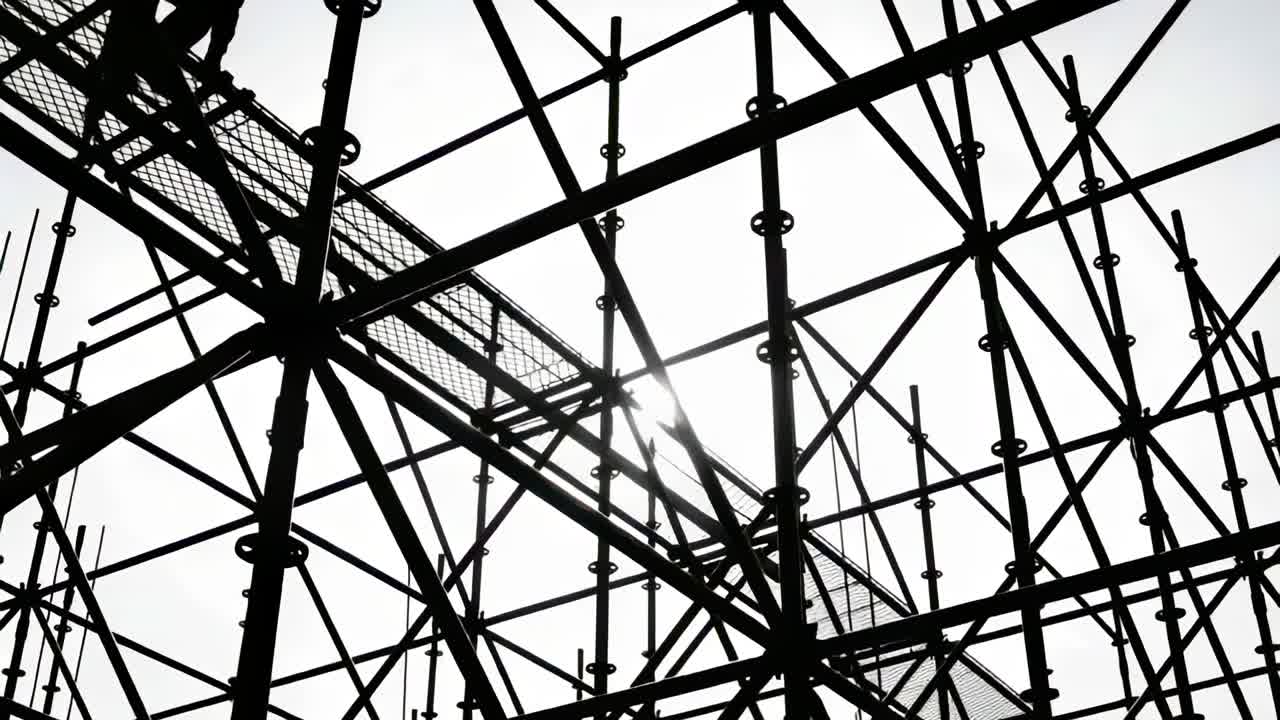 Shifting camera revealing sunlit scaffold on site while worker climbing grated platform inspecting