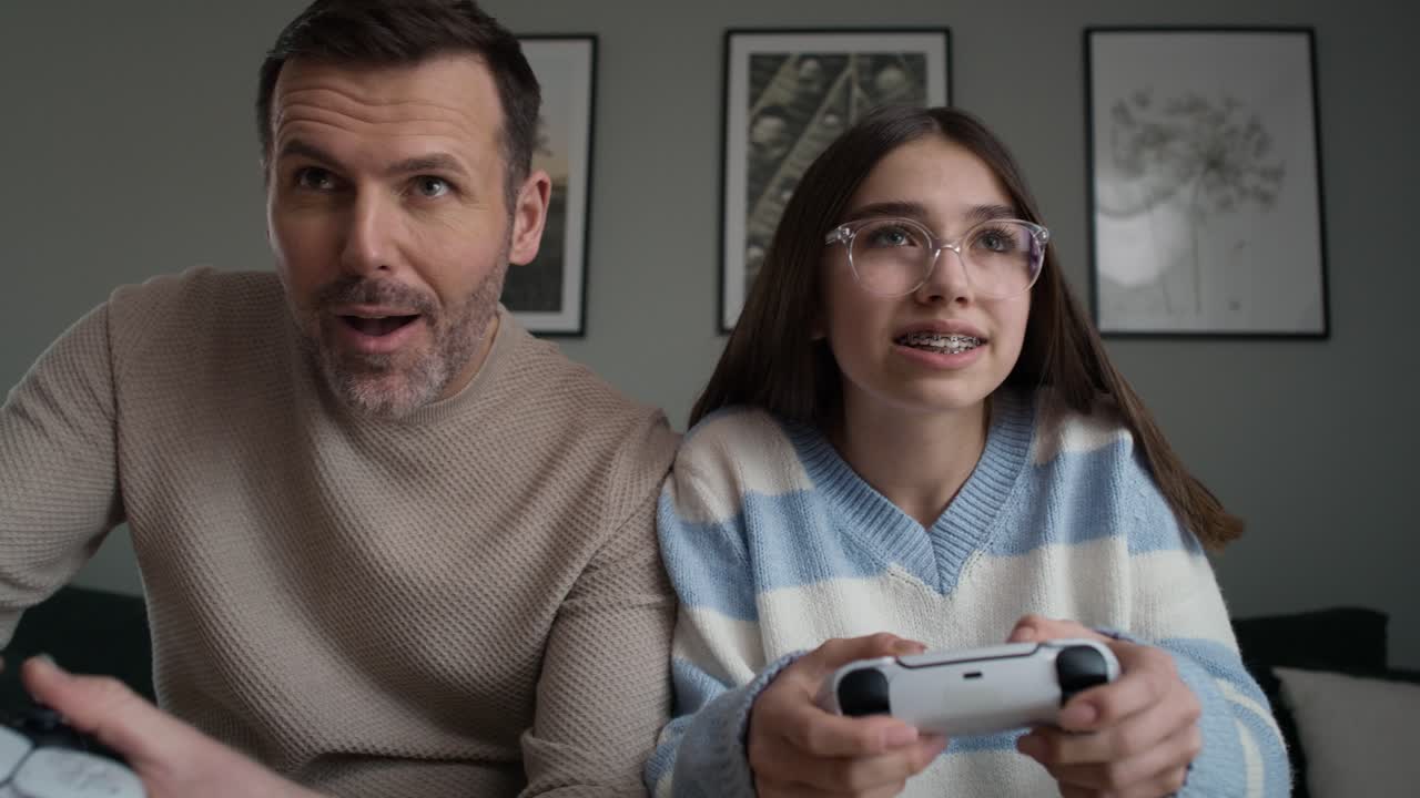 vista frontal de una adolescente caucásica y su padre jugando a un videojuego con un controlador de juego