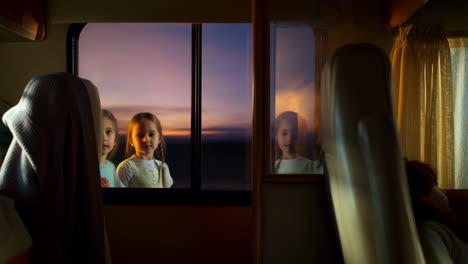 young girls looking out rv window at sunset