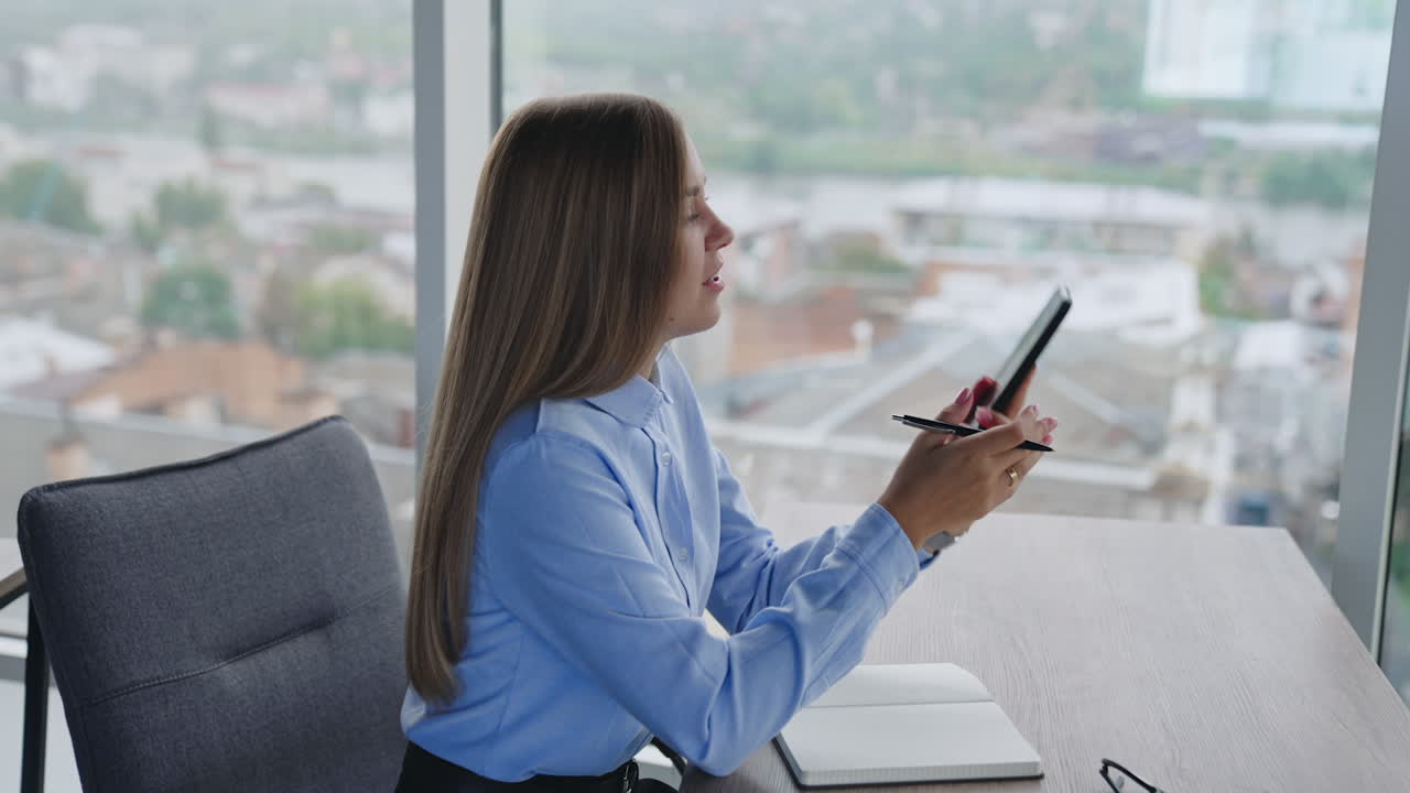 Business lady sits at desk and speaks on the phone. Woman finishes her conversation and puts the phone on the table.