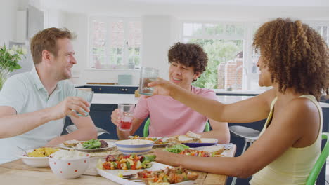 Familia-Multirracial-Con-Un-Hijo-Adolescente-Sentado-Alrededor-De-Una-Mesa-En-La-Cocina-De-Casa-Comiendo-Juntos