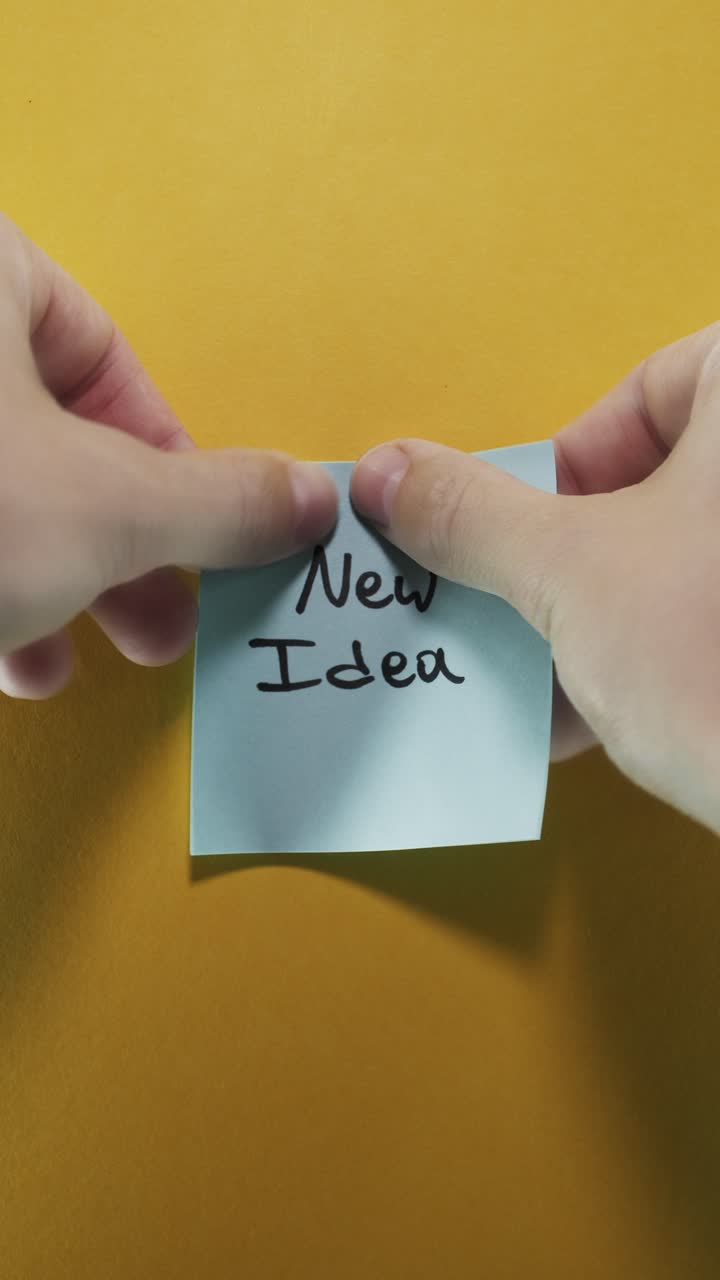 Portrait shot of a blue sticky note reading "New Idea" on a yellow background