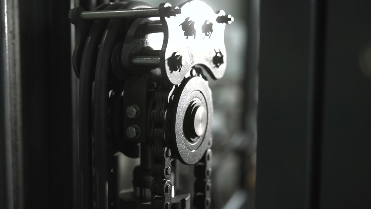 Detail mechanismu řetězového kola pod vysoce kontrastním osvětlením, pohybující se články a válečky, drsné prostředí dílny.