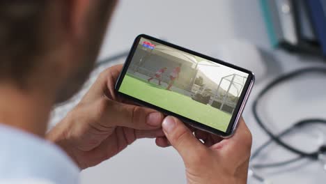 compuesto de un médico masculino viendo un partido de hockey en un teléfono inteligente
