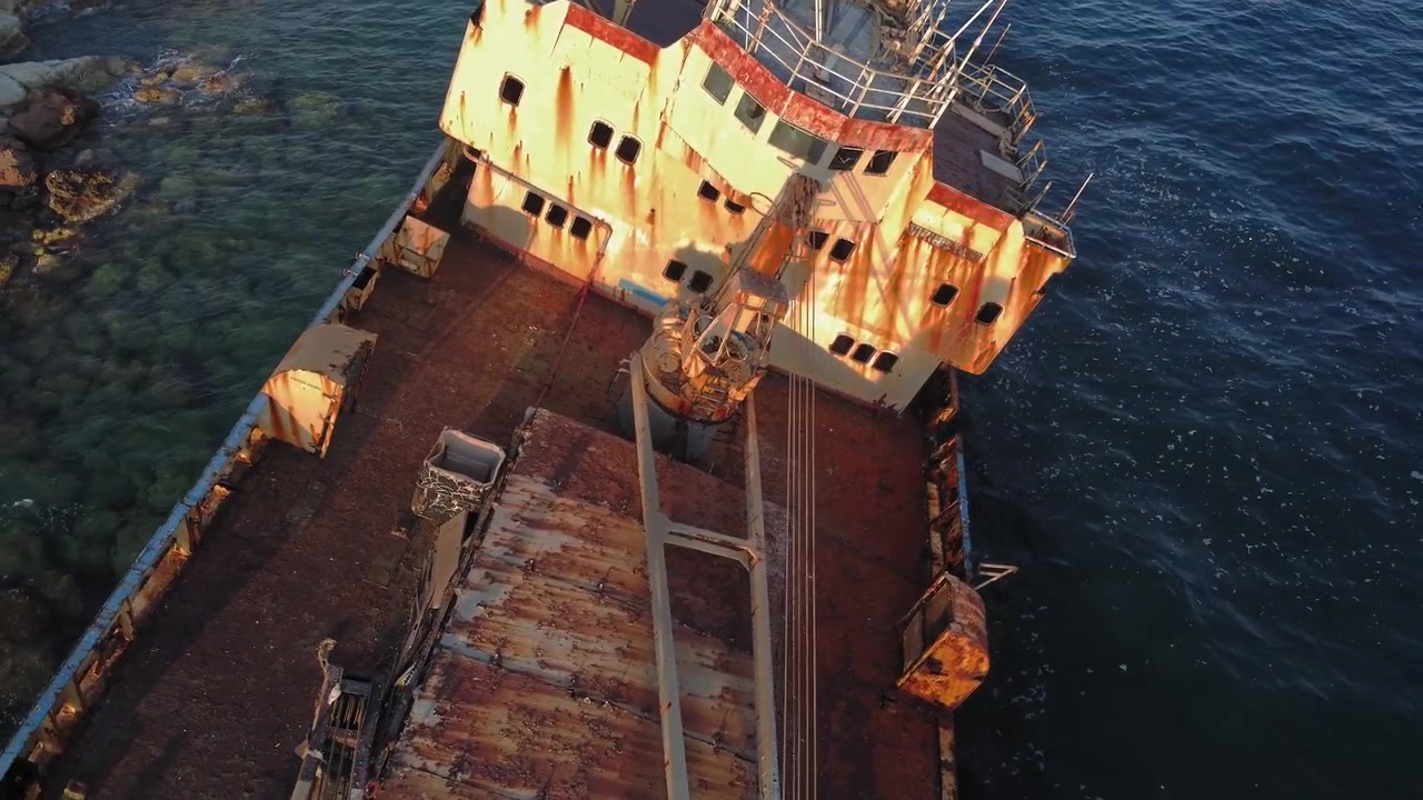 Aerial view of a rusted abandoned ship grounded on rocks near the sea showing decay and maritime